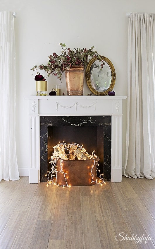 classic fake fireplace with string lights covering birch logs